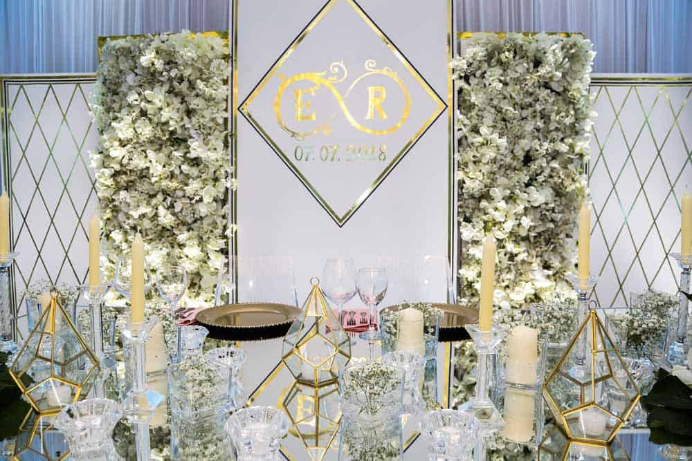 Elegant wedding reception centerpiece with white floral arrangements and gold accents in a luxurious venue setting.