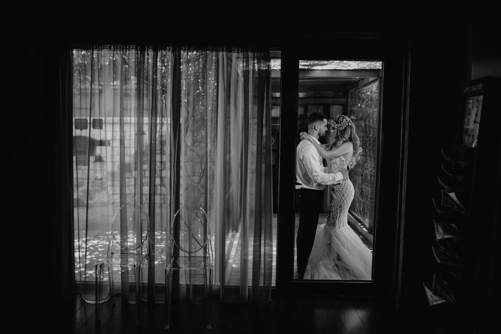Elegant black-and-white photo of a bride and groom reminiscing inside a luxurious high-end wedding venue, highlighting intimacy and sophisticated decor.