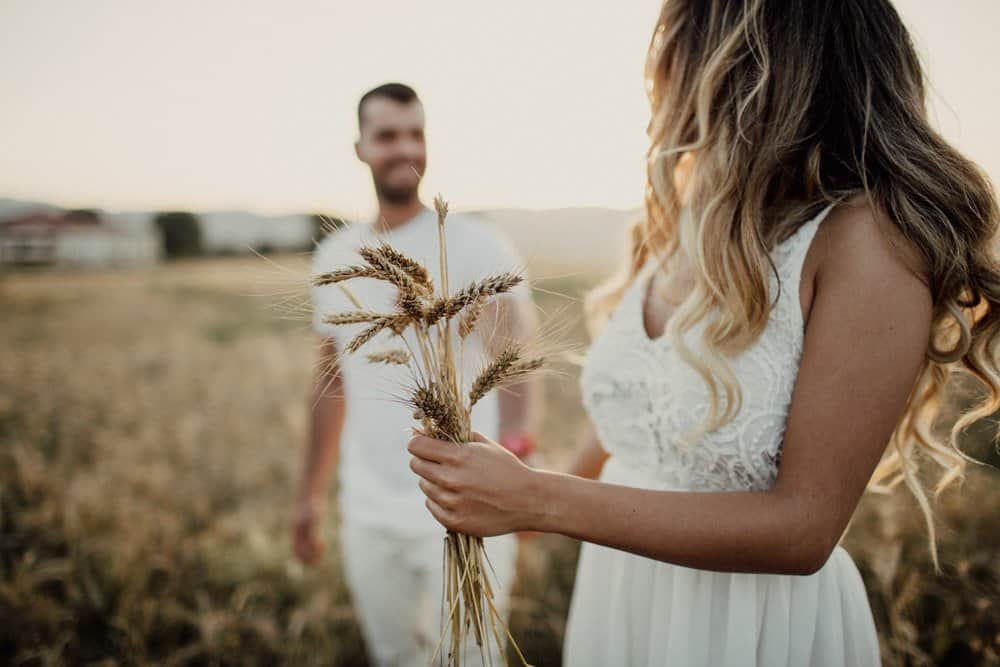 Elegant bride holding dried floral bouquet in golden sunset field for luxury wedding photoshoot.