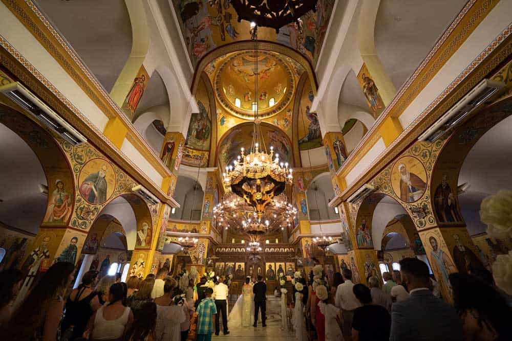 Luxurious wedding ceremony inside an ornate high-end church with stunning chandeliers and intricate religious murals.