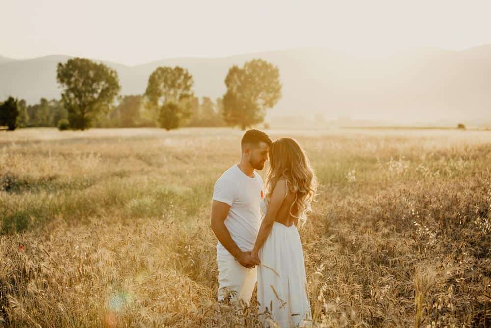 Romantic couple holding hands in a golden wheat field at sunset, perfect for luxury wedding photography, high-end outdoor wedding venues.