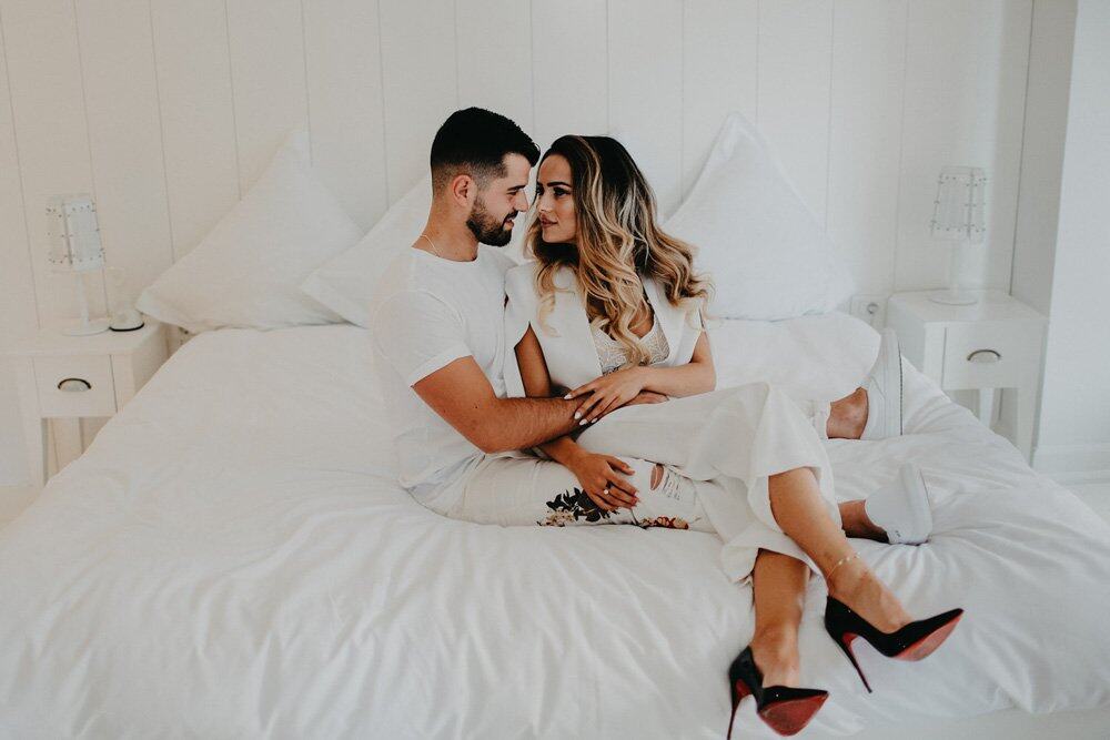 Elegant couple embracing on a luxurious white bed in a high-end wedding venue, showcasing romance and sophistication.