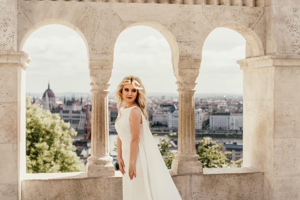 Elegant bride in a white wedding gown on a historic terrace overlooking a European city skyline, perfect for luxury weddings.