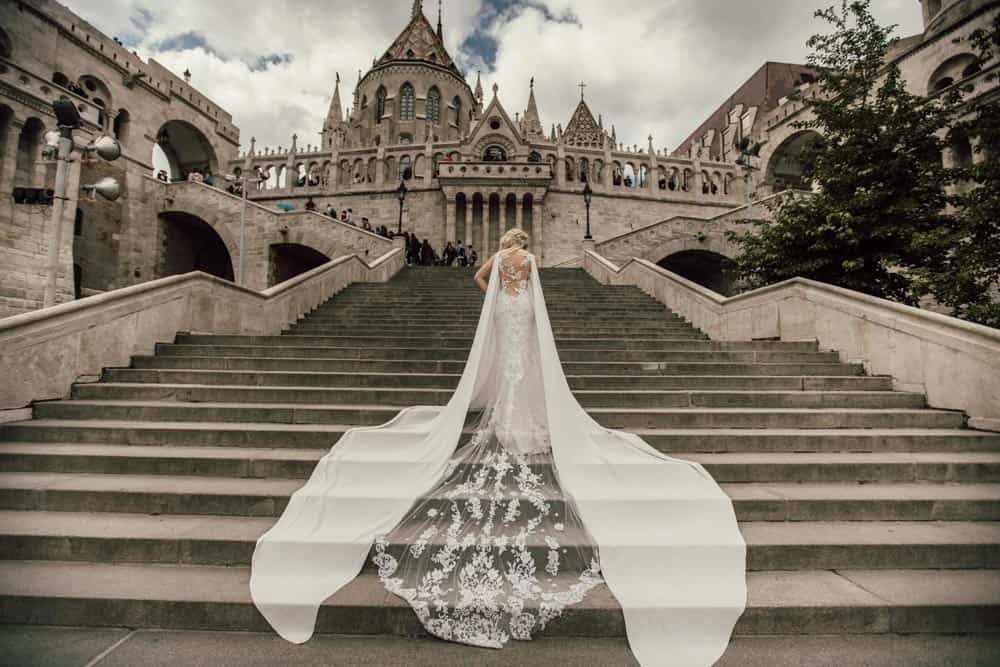 Elegant bride in a luxurious wedding gown ascending the historic Fisherman's Bastion stairs in Budapest, showcasing high-end wedding fashion in a picturesque setting.