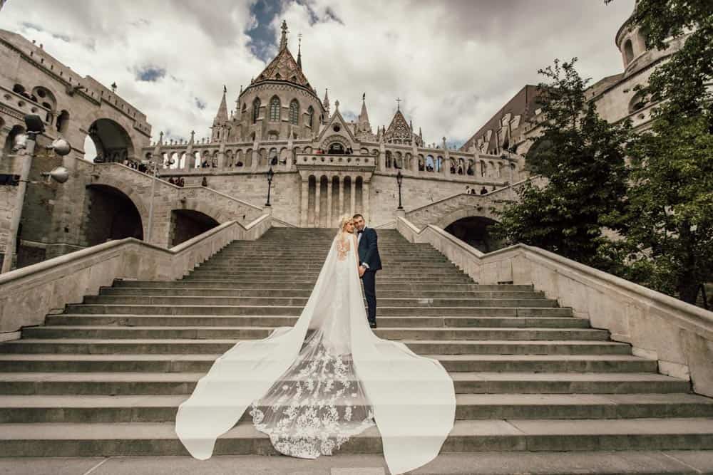 Luxurious wedding couple on historic castle stairs with dramatic sky.
