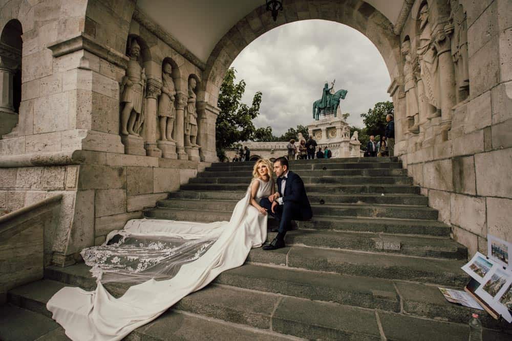 Luxury wedding couple at Buda Castle in Budapest, ornate stone architecture and iconic statues, romantic high-end wedding photography capturing elegance and timeless beauty.