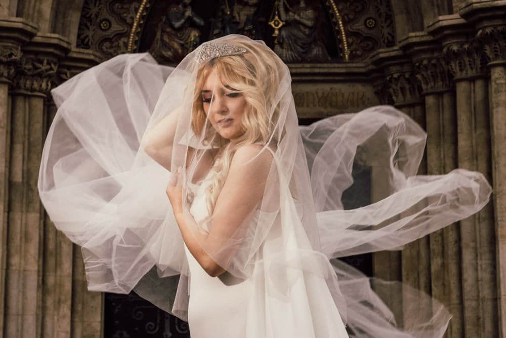 Elegant bride with flowing tulle veil in an ornate historic church setting, capturing a luxurious wedding moment.