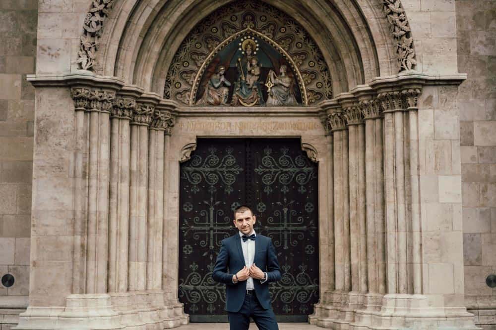 Elegant groom in a navy tuxedo standing in front of a historic church entrance, perfect for luxury wedding photography.