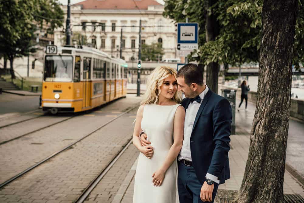 Elegant bride and groom in city street with tram, romantic wedding photo in downtown urban setting.