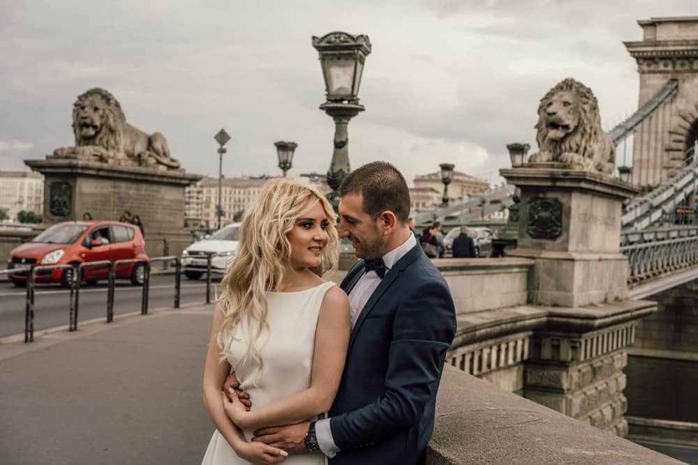 Elegant bride and groom posing near historic bridge and lion statues in a luxurious city wedding setting.