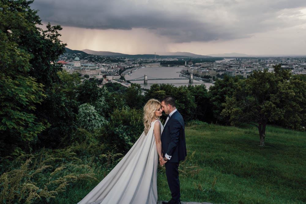 Elegant bride and groom sharing a moment with a scenic city view of Budapest and the Danube River in the background during a luxurious wedding photoshoot.