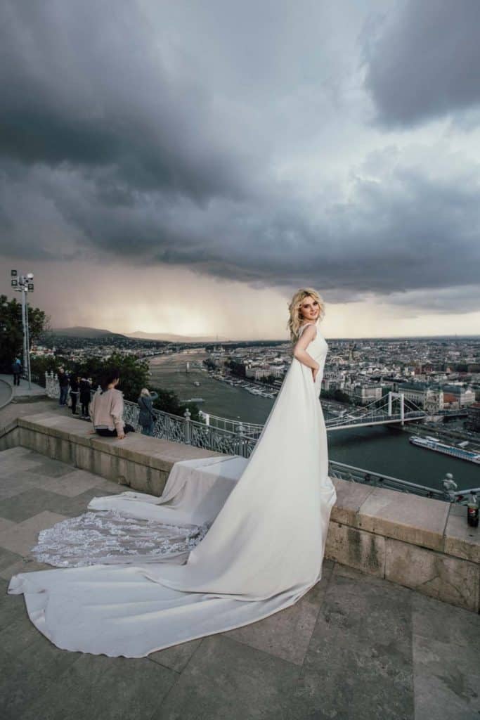 Elegant bride in a stunning white wedding dress overlooking a city skyline at sunset, perfect for luxury wedding venues.