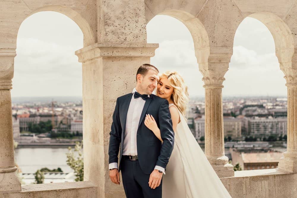 Elegant bride and groom sharing a romantic moment on a historic rooftop with a panoramic city view.