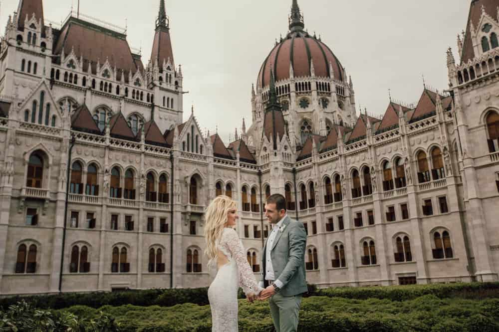 Elegant couple at a luxury wedding venue in front of a historic castle with intricate architecture and grand towers.