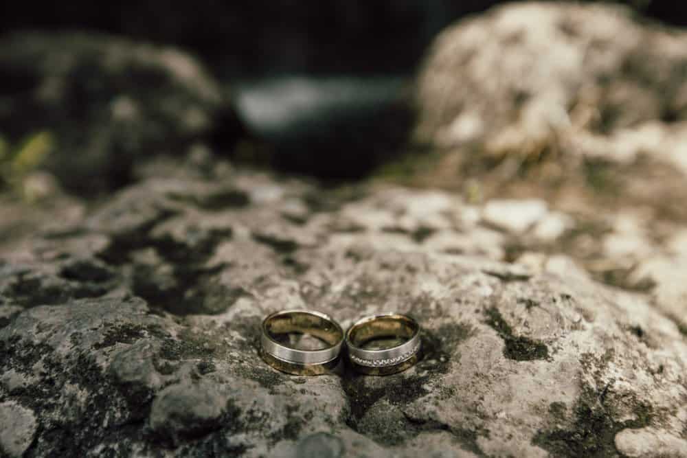 Gold wedding rings on a textured stone surface in an outdoor setting.