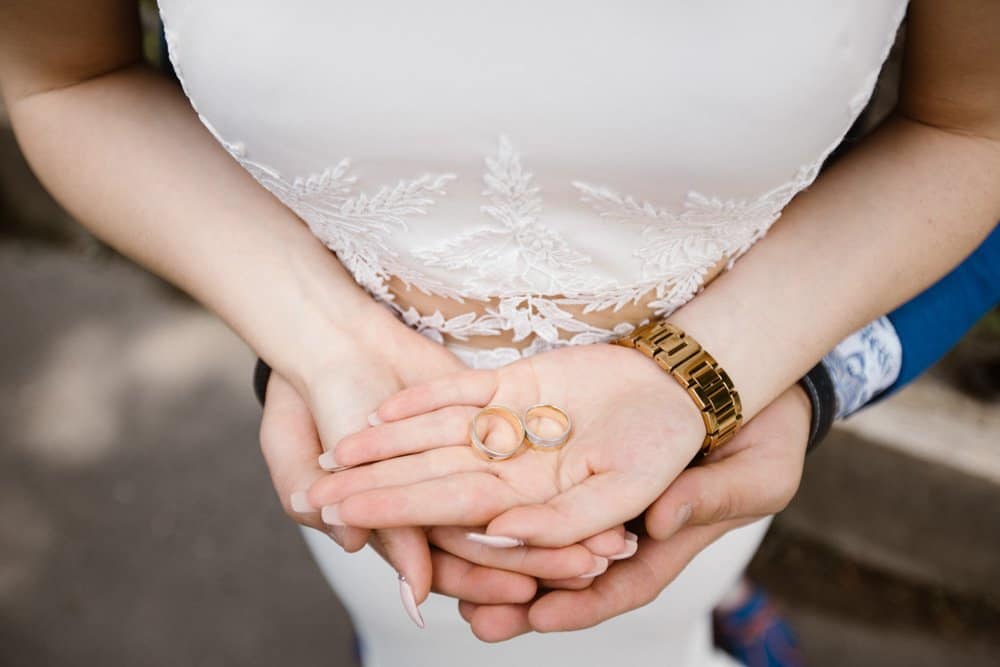 Elegant wedding rings held by a bride with a lace wedding dress and a gold watch, symbolizing love and commitment at a luxurious wedding venue.