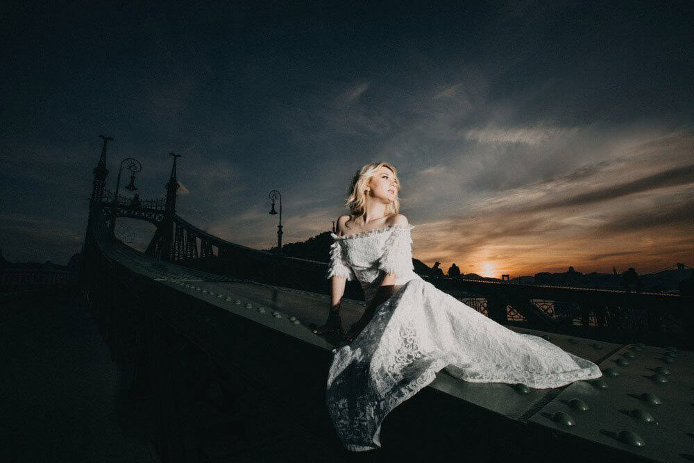 Luxury bride in elegant wedding gown on historic bridge during sunset.