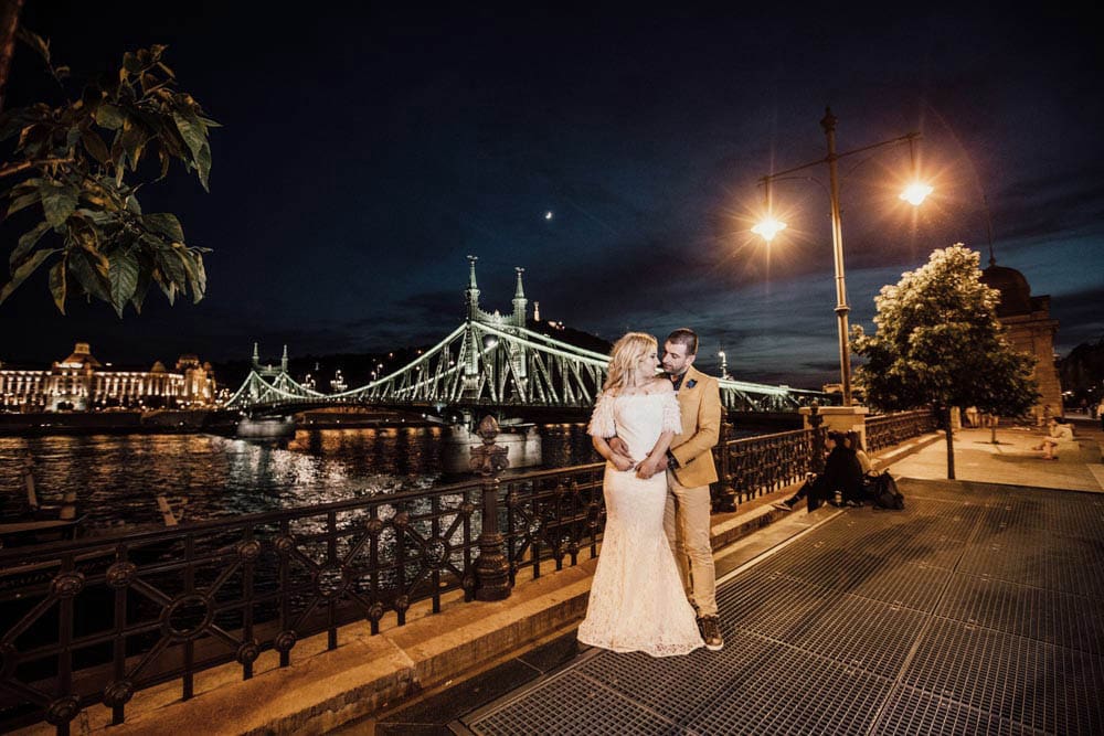Elegant couple kissing by the Danube River at night, showcasing a luxurious wedding photoshoot in Budapest’s high-end cityscape.