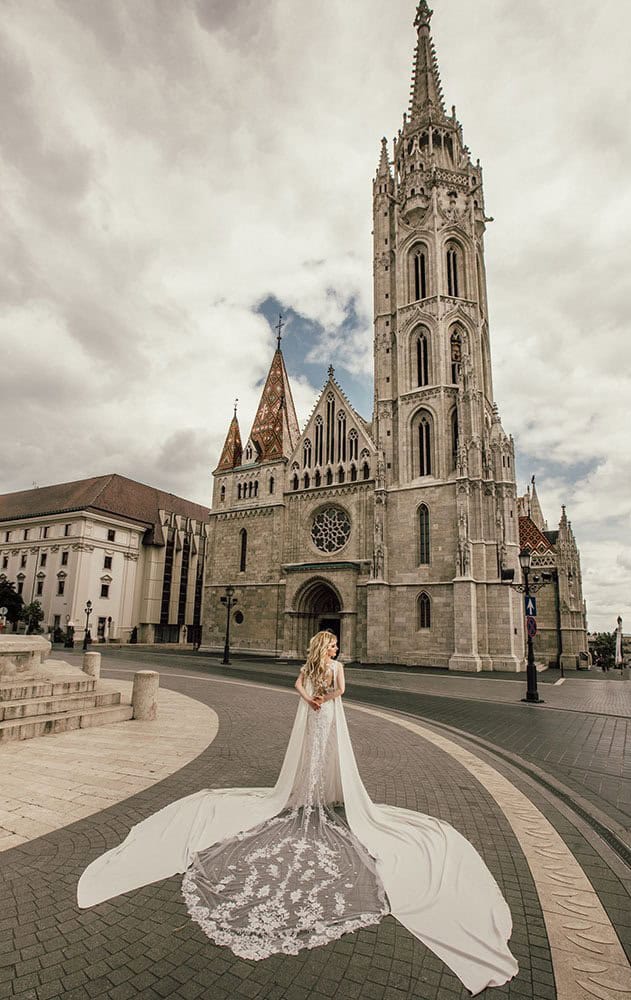 Elegant wedding dress with a dramatic train in front of a historic cathedral for a luxury wedding photoshoot.