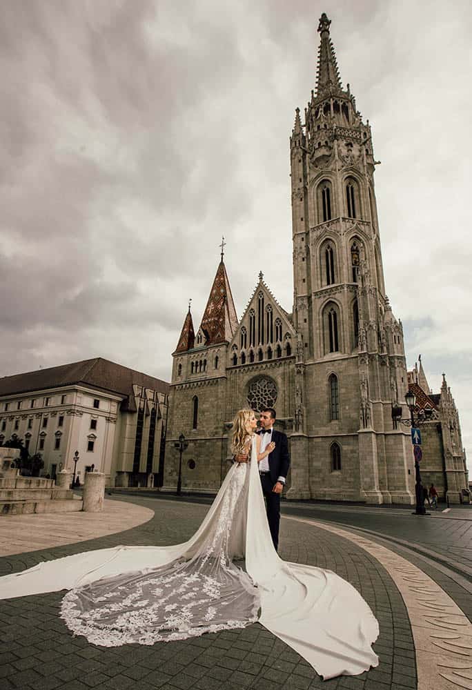 Elegant wedding couple in front of historic Gothic cathedral, perfect high-end venue for a luxury wedding celebration.
