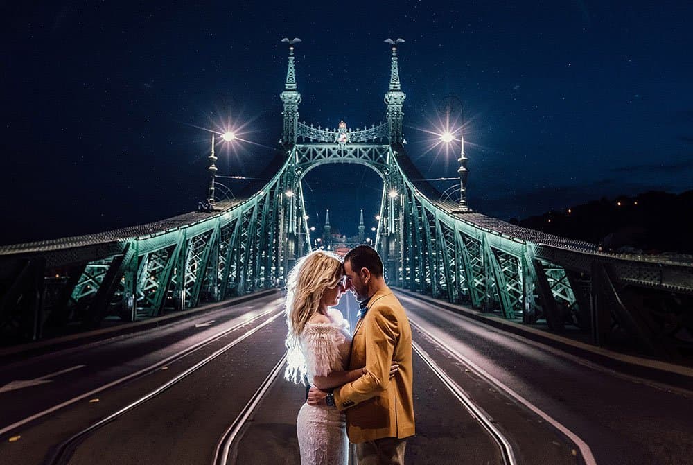 Elegant couple sharing a romantic moment beneath a beautifully lit bridge at night, ideal for a luxury wedding photoshoot.
