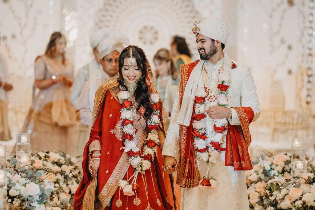 Elegant Indian couple during traditional wedding ceremony in luxurious venue, surrounded by floral arrangements and ornate decor, capturing love and cultural richness.