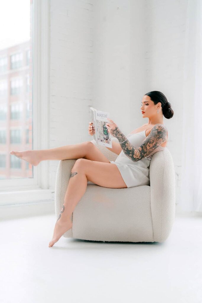 Elegant bride with tattoos reading in a bright, modern indoor space, showcasing luxury wedding preparations.