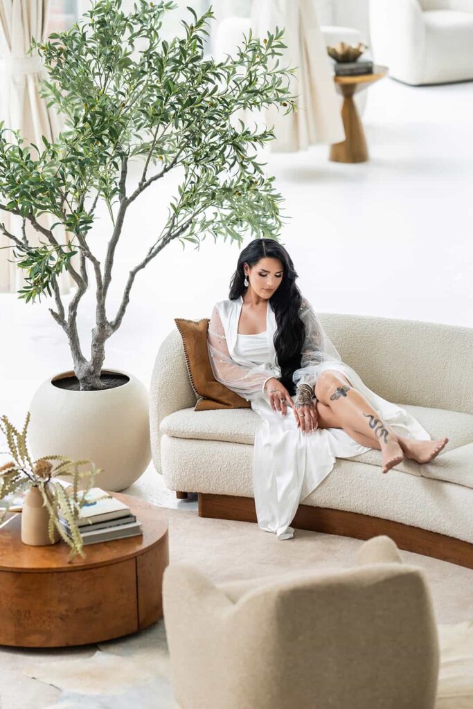 Elegant bride relaxing on a luxurious modern sofa with green foliage in a high-end wedding venue.