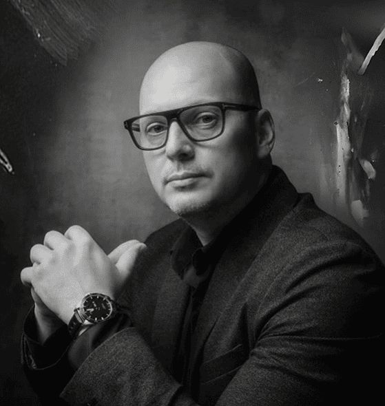 Professional wedding photographer portrait wearing glasses, black suit, high-end photography studio, luxury wedding lighting, creative wedding photography, elegant wedding photos, modern wedding videography, exclusive wedding venue, refined wedding imagery, sophisticated wedding moments.