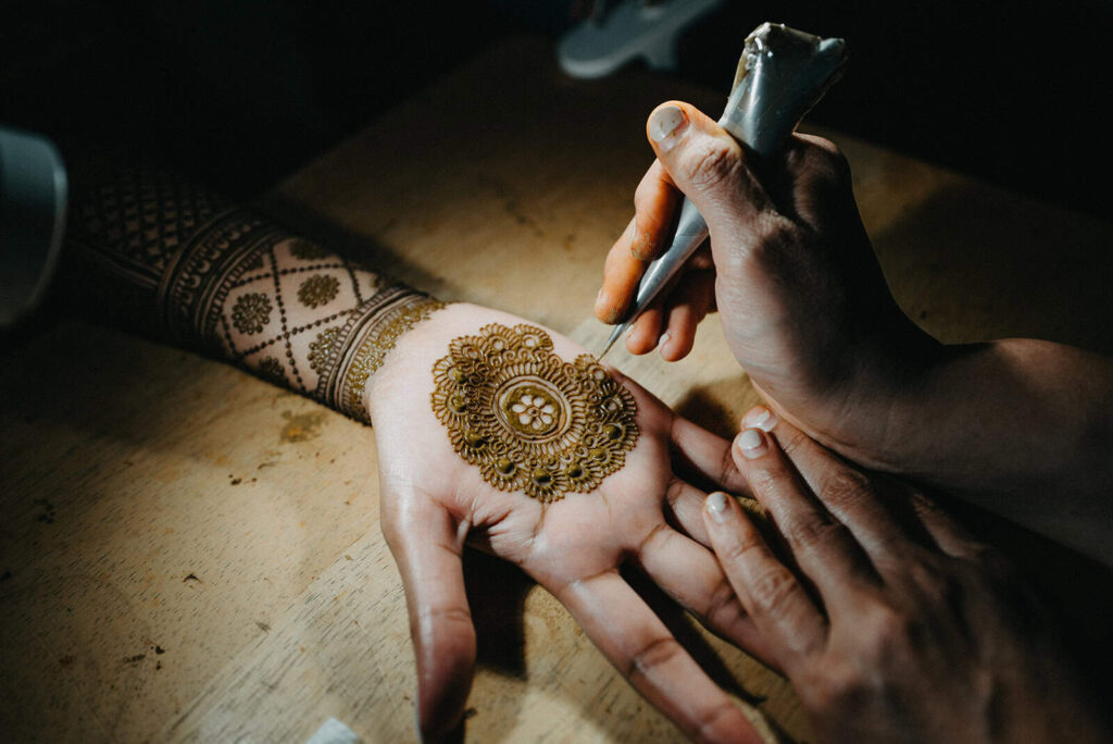 Intricate henna design being applied to a bride's hand for a luxurious wedding celebration.