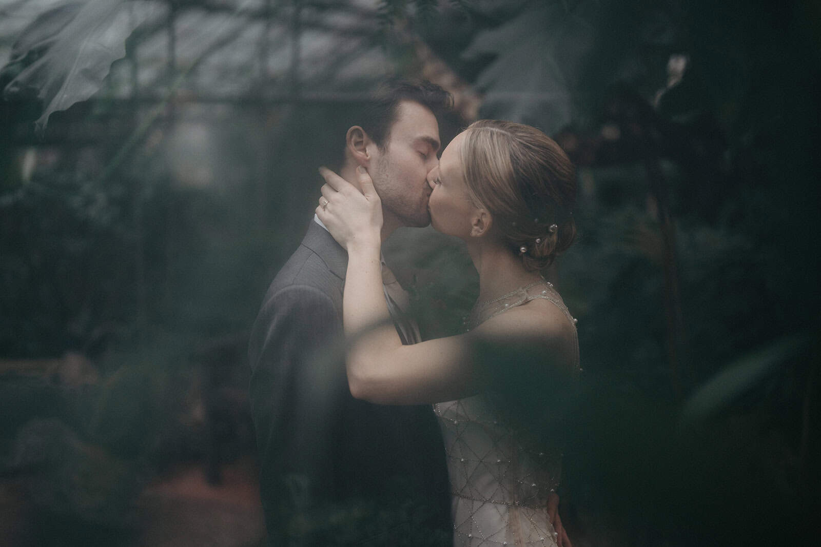 Romantic couple sharing a kiss at an elegant wedding in a lush garden setting.