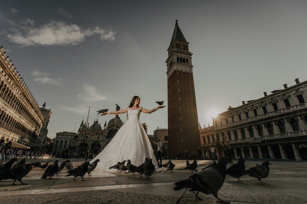 Elegant bride in wedding gown feeding pigeons in Piazza San Marco, Venice, during sunset, showcasing a luxurious romantic wedding setting.