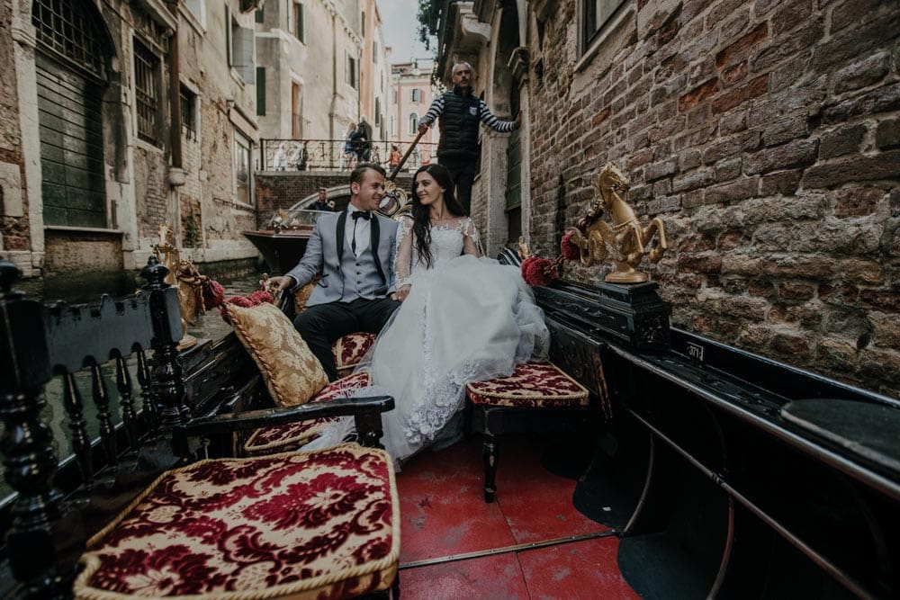 Charming couple in wedding attire on an elegant gondola ride through Venice's romantic canals.