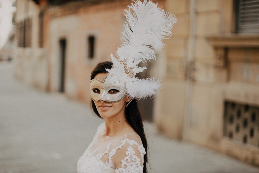 Elegant bride wearing a luxurious wedding dress and ornate mask with feathers, during a high-end wedding celebration.