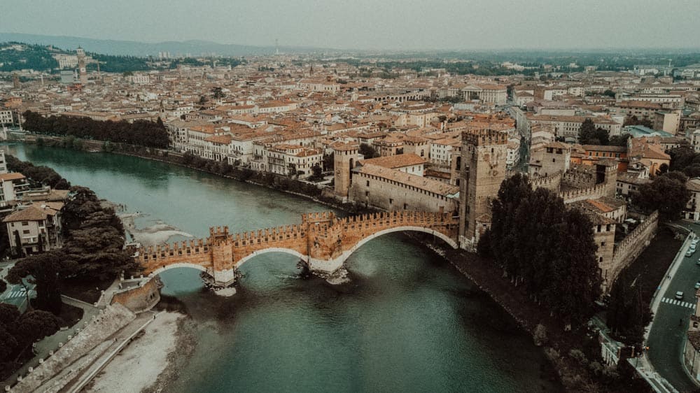 Vintage aerial view of a historic Italian city with a bridge over the river, showcasing high-end venues and luxurious wedding settings.