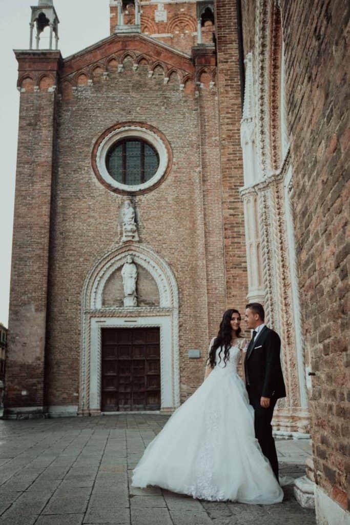 Elegant bride and groom in front of historic brick church, perfect for luxury wedding venues.