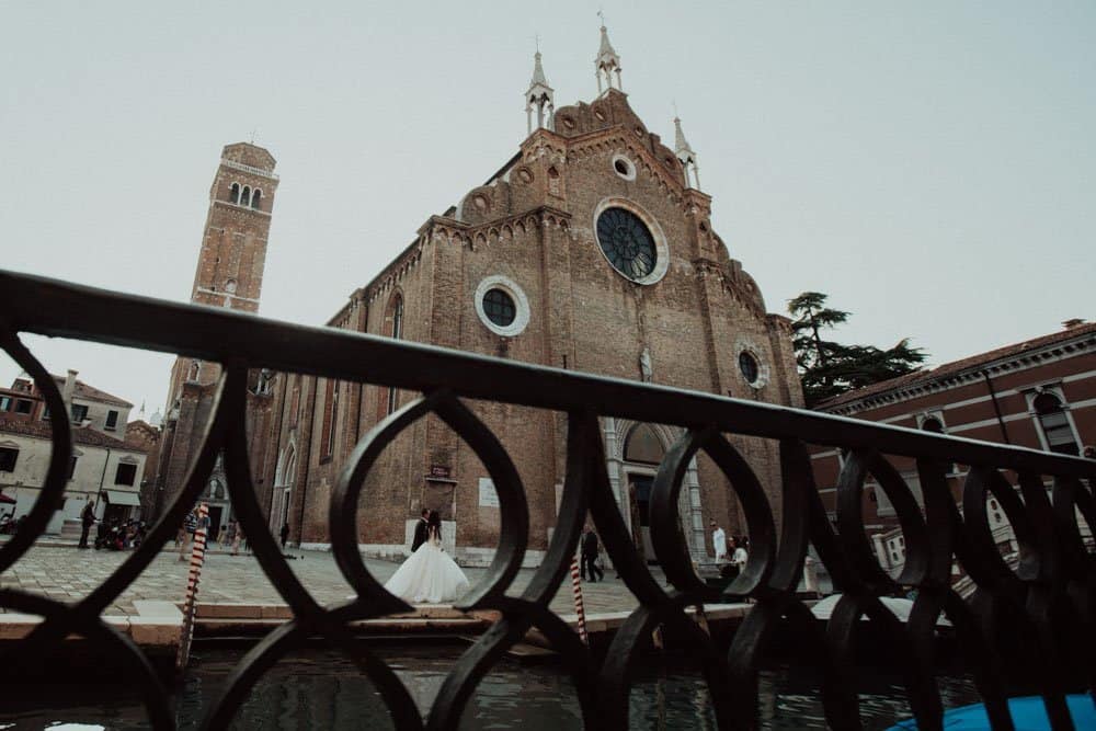 Elegant bride in wedding dress on canal bridge near historic church, Venice, Italy.