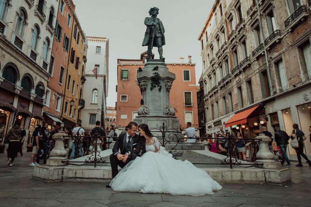 Luxurious wedding couple sitting in historic city square, high-end wedding venue, romantic cityscape background, elegant wedding attire, romantic destination wedding, Italy.