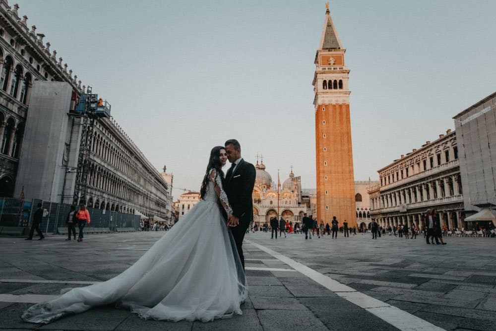 Elegant bride and groom in Venice's Piazza San Marco with historic architecture and iconic clock tower.