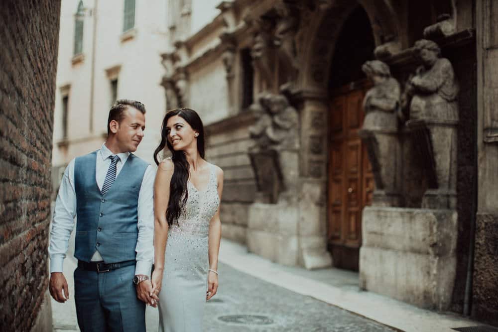 Elegant couple walking through historic city street, perfect for luxury wedding photography, showcasing timeless romance and high-end venue ambiance.