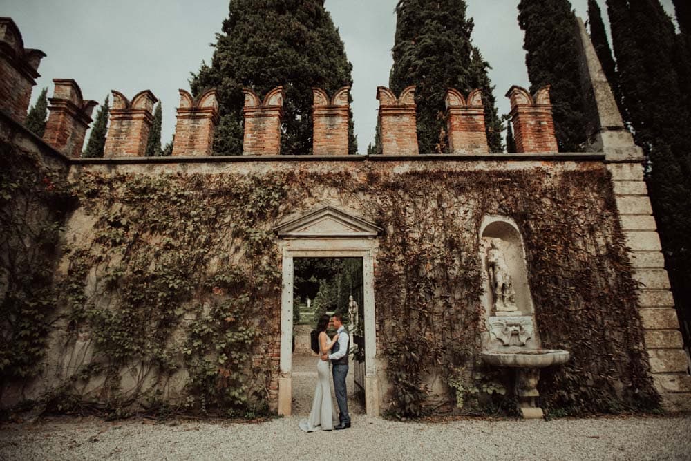 Elegant couple at an ornate historic venue with lush greenery and classical architecture, perfect for luxury weddings.