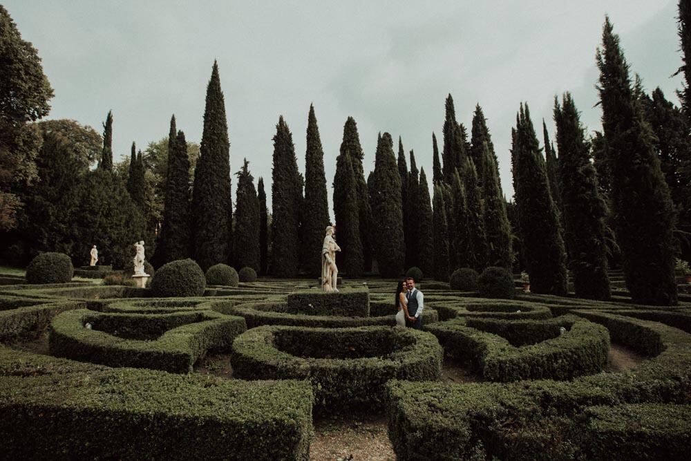 Luxurious wedding couple in elegant attire at a formal garden with manicured hedges and classical statues, perfect for high-End wedding photography.