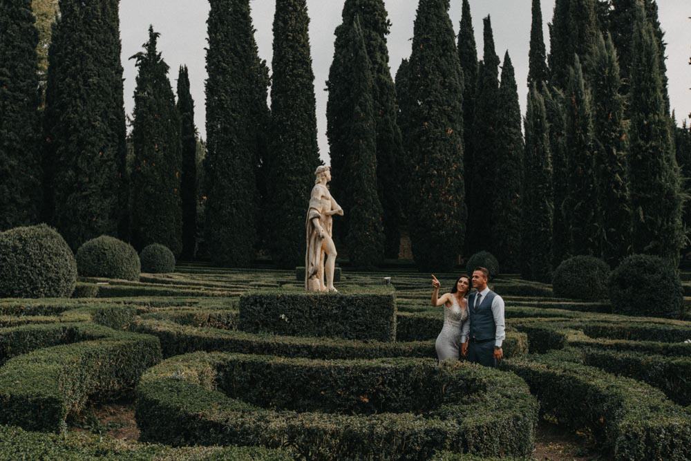 Luxurious couple in elegant attire enjoying a romantic moment in a beautifully manicured garden at a high-end venue.