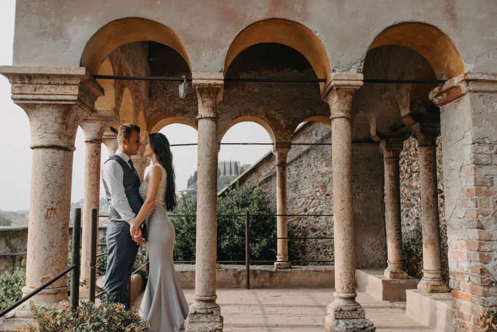 Elegant wedding couple standing beneath historic stone arches at a luxurious venue in Italy.
