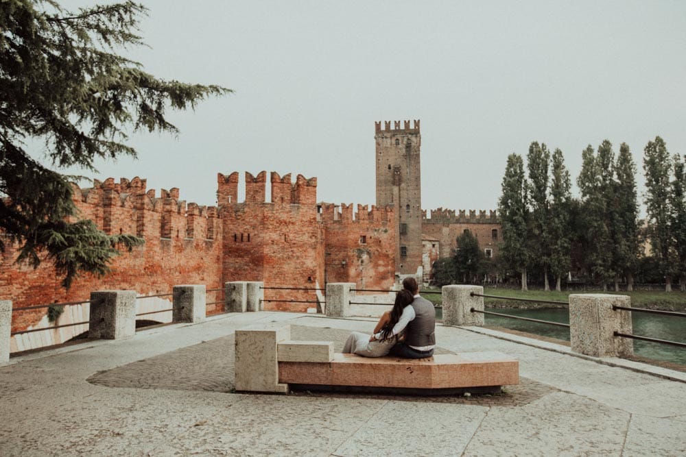 Elegant couple sitting on a modern bench with a historic castle backdrop, highlighting luxury wedding venues.