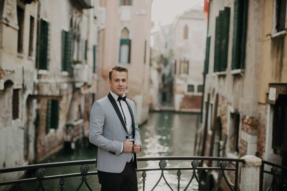 Venetian canal wedding scene with elegant groom in a tailored gray tuxedo overlooking a historic canal.