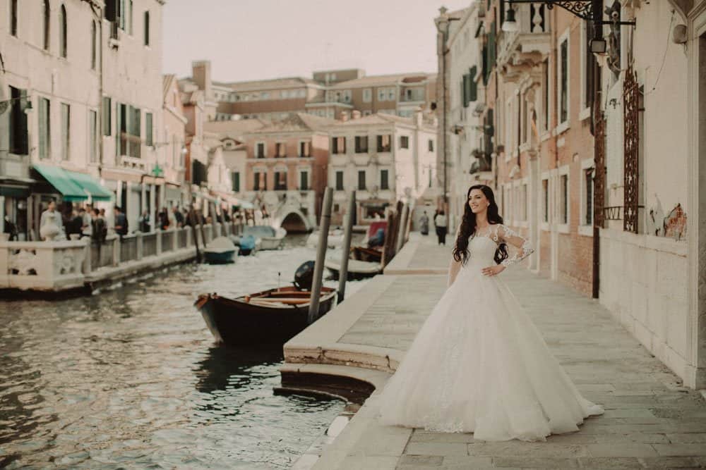 Elegant bride in a romantic wedding dress along Venice canal with historic architecture and gondolas.