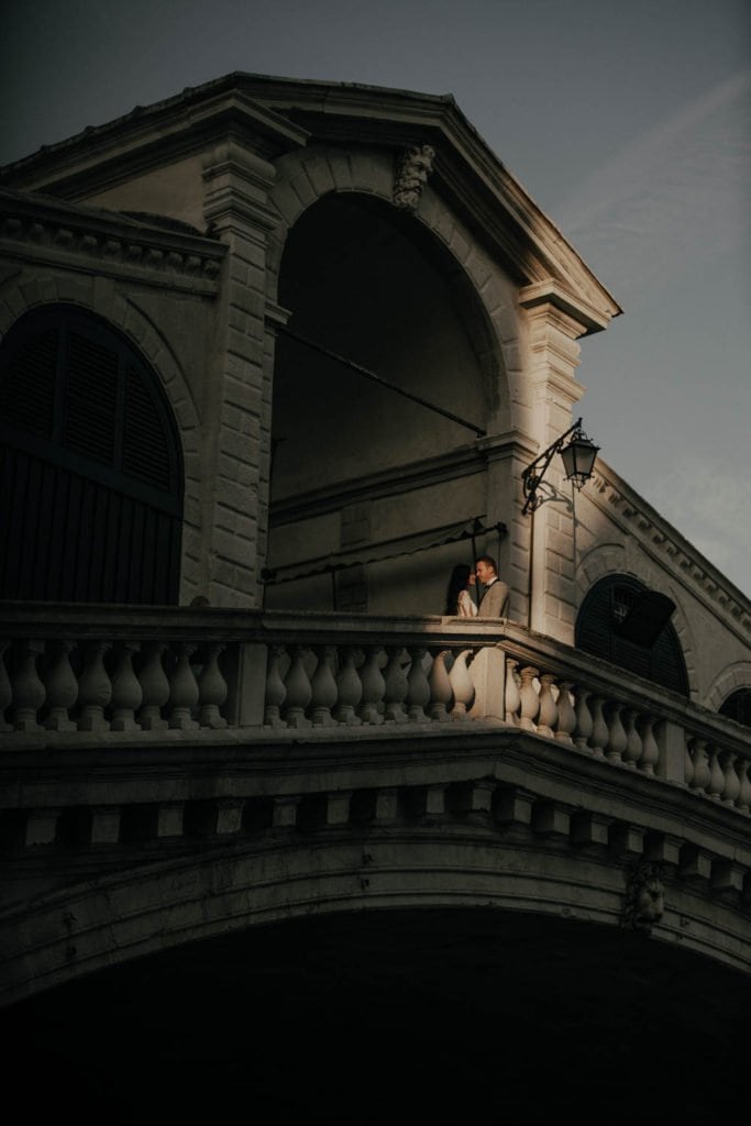Elegant couple sharing a moment on a grand historic balcony at dusk, perfect for luxury wedding venues and high-end event photography.