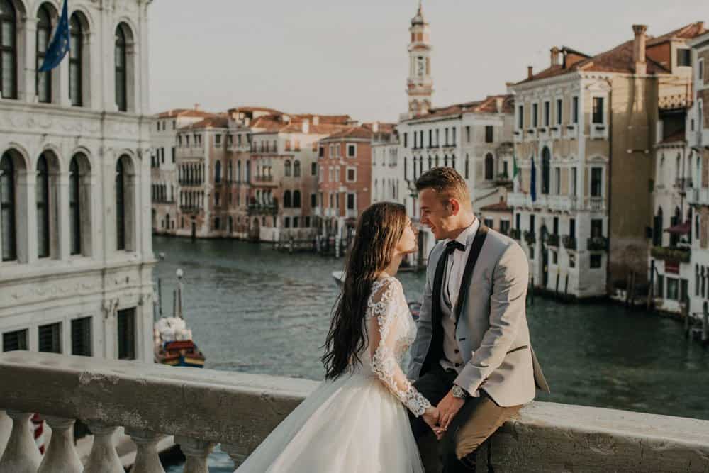 Venetian couple in wedding attire on a scenic bridge overlooking canals in Venice, Italy.