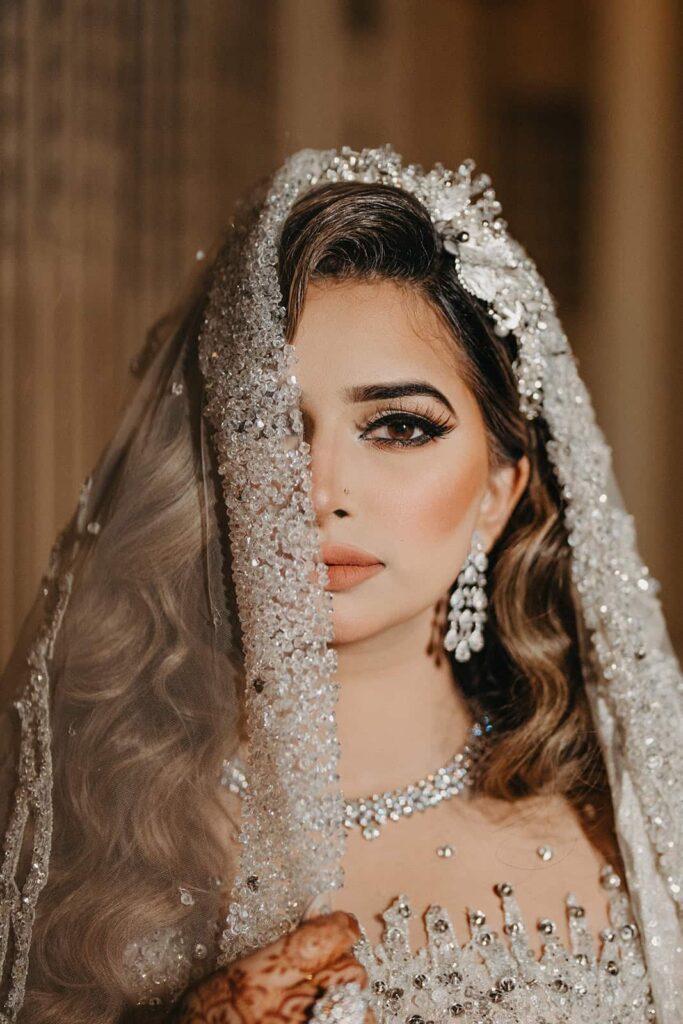 Elegant bridal portrait with intricate jewelry, luxurious veil, and glamorous makeup at a high-end wedding venue.